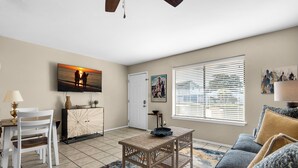 A living room with a dining area, a sofa, a coffee table, and a TV mounted on the wall. - Sandprints A1 (Miramar Beach)