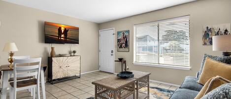 A living room with a dining area, a sofa, a coffee table, and a TV mounted on the wall.