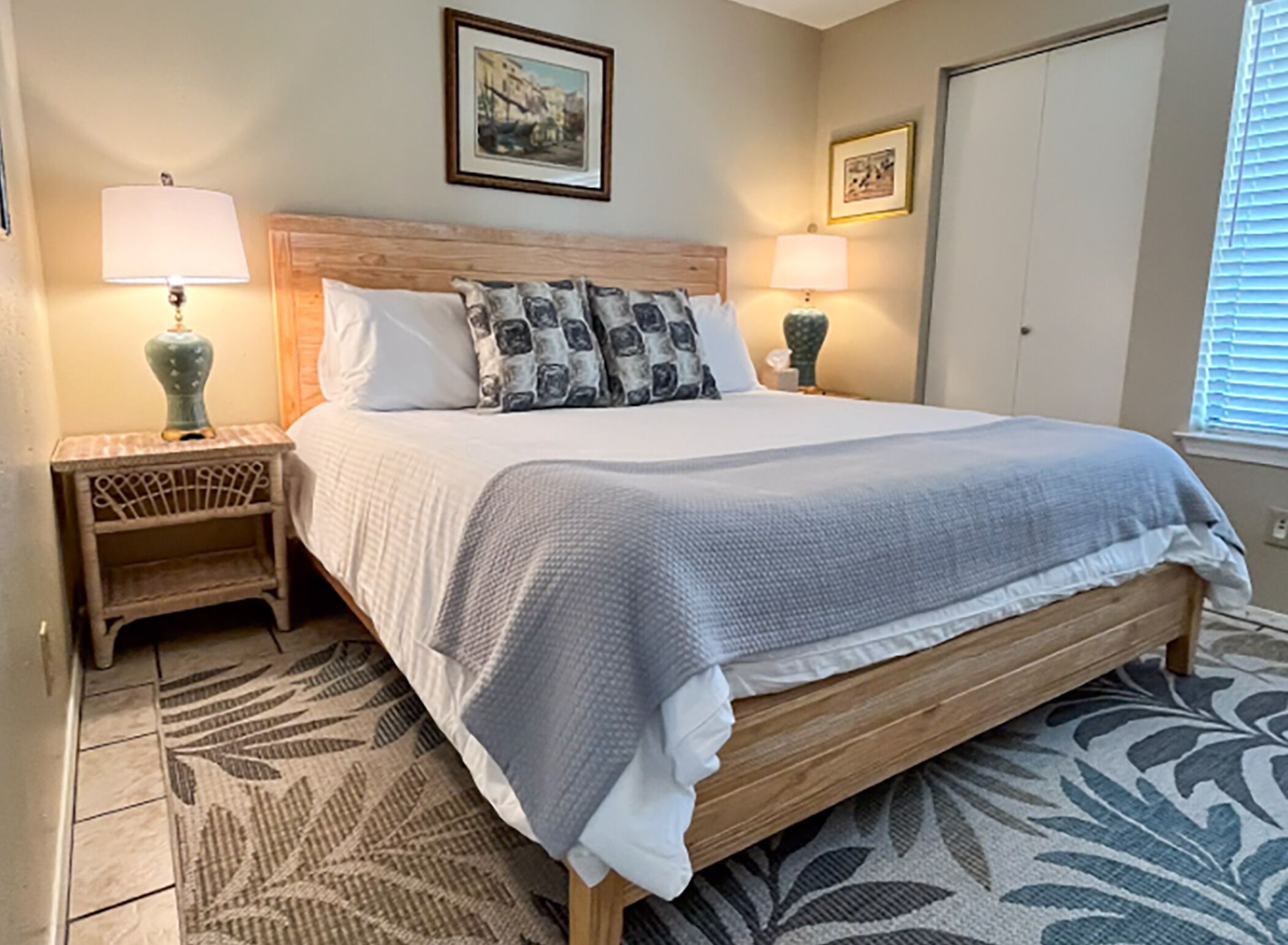A neatly arranged bedroom with a wooden bed, two bedside lamps, a patterned rug, and framed pictures on the walls.