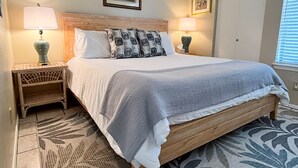 A neatly arranged bedroom with a wooden bed, two bedside lamps, a patterned rug, and framed pictures on the walls. - Sandprints A1 (Miramar Beach)