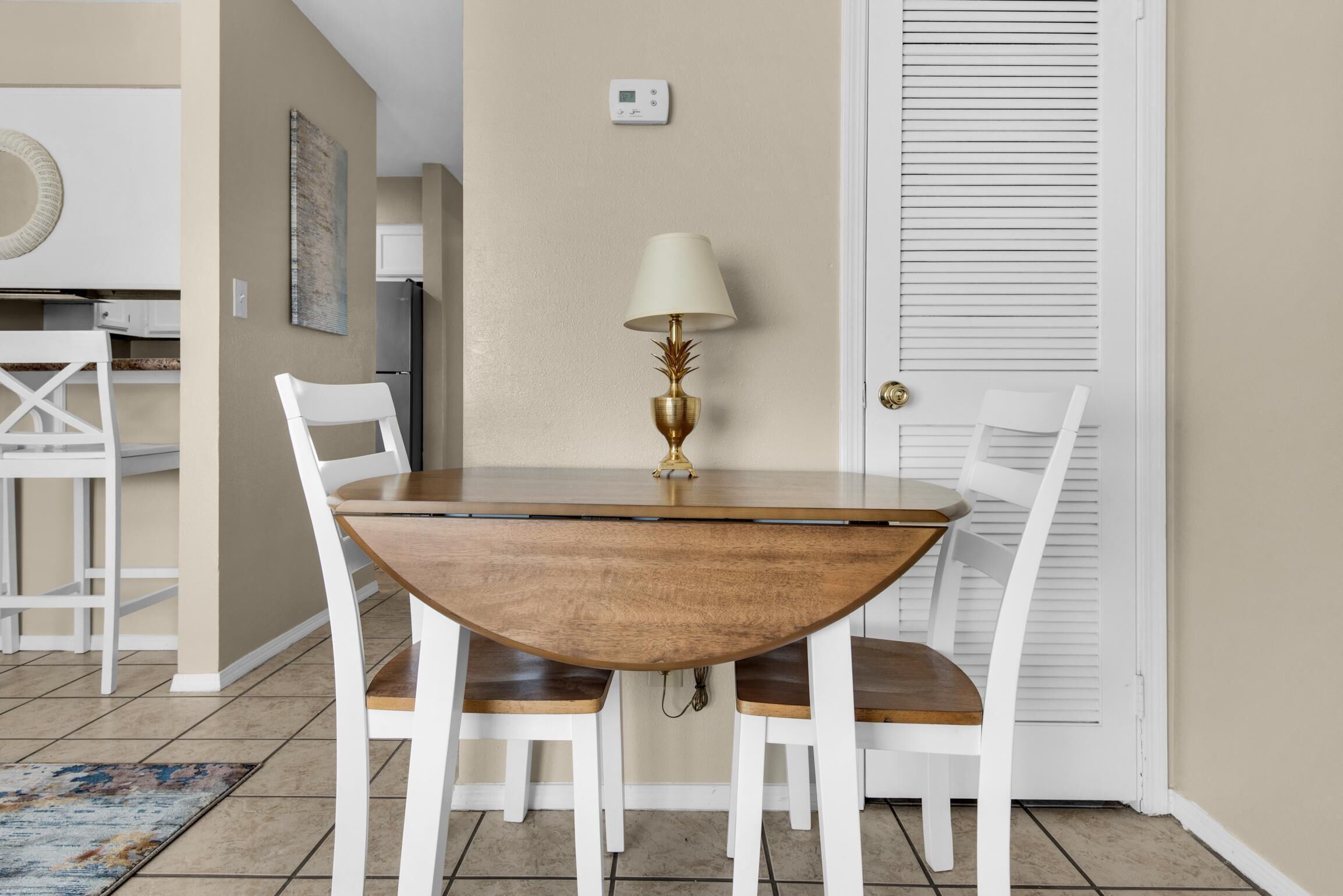 Un coin repas avec une table ronde en bois, des chaises blanches et une lampe dorée.