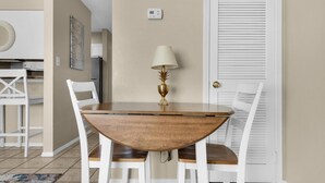 A dining area with a round wooden table, white chairs, and a gold lamp. - Sandprints A1 (Miramar Beach)