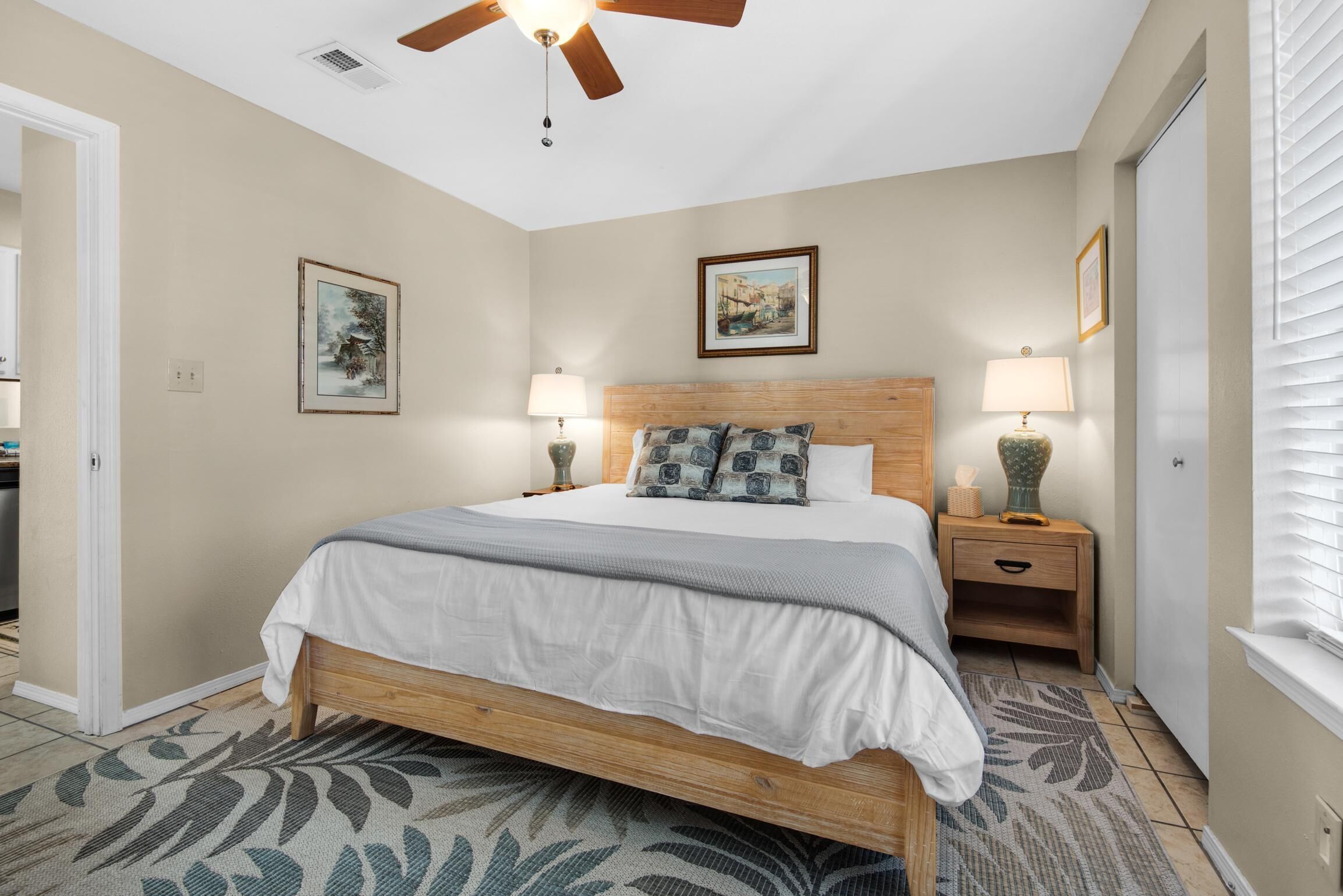 A bedroom with a wooden bed, two bedside tables with lamps, a ceiling fan, and framed artwork on the walls.