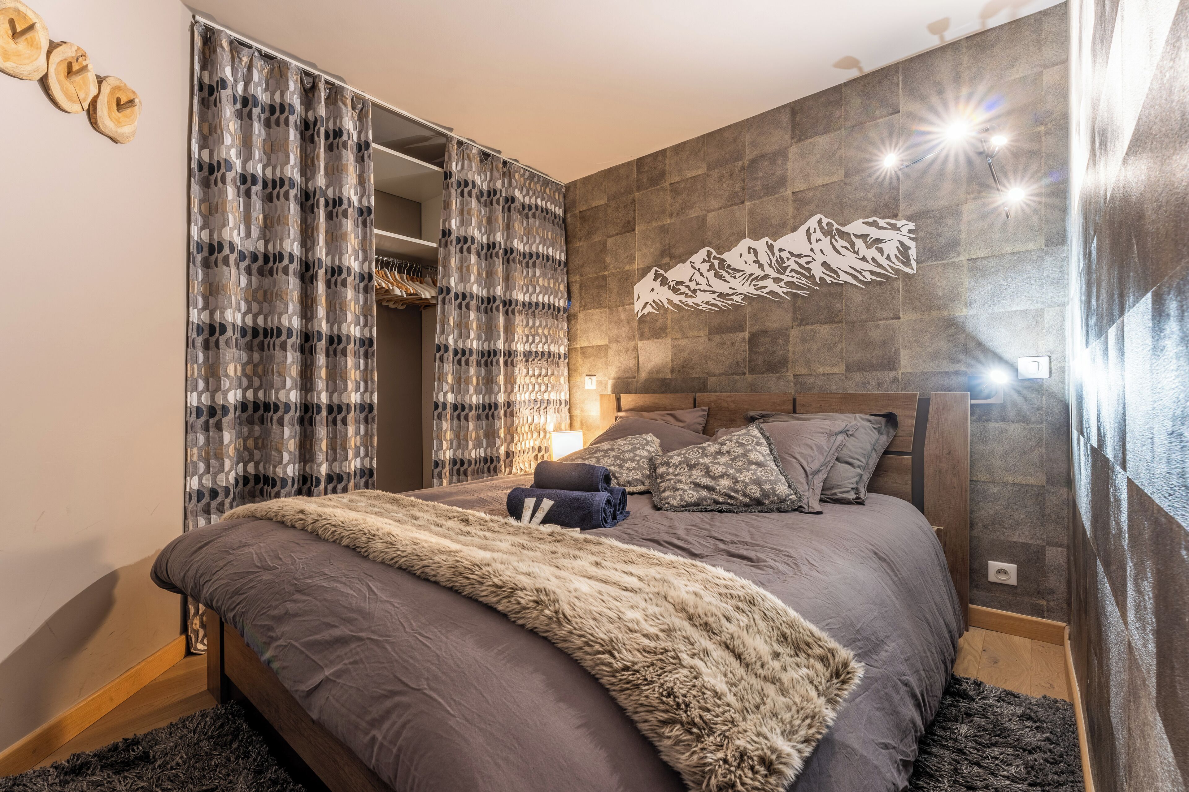 A modern bedroom with a large bed, a wardrobe, and a decorative wall piece.