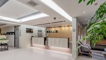 A modern hotel lobby with a reception desk, seating area, and a large plant.