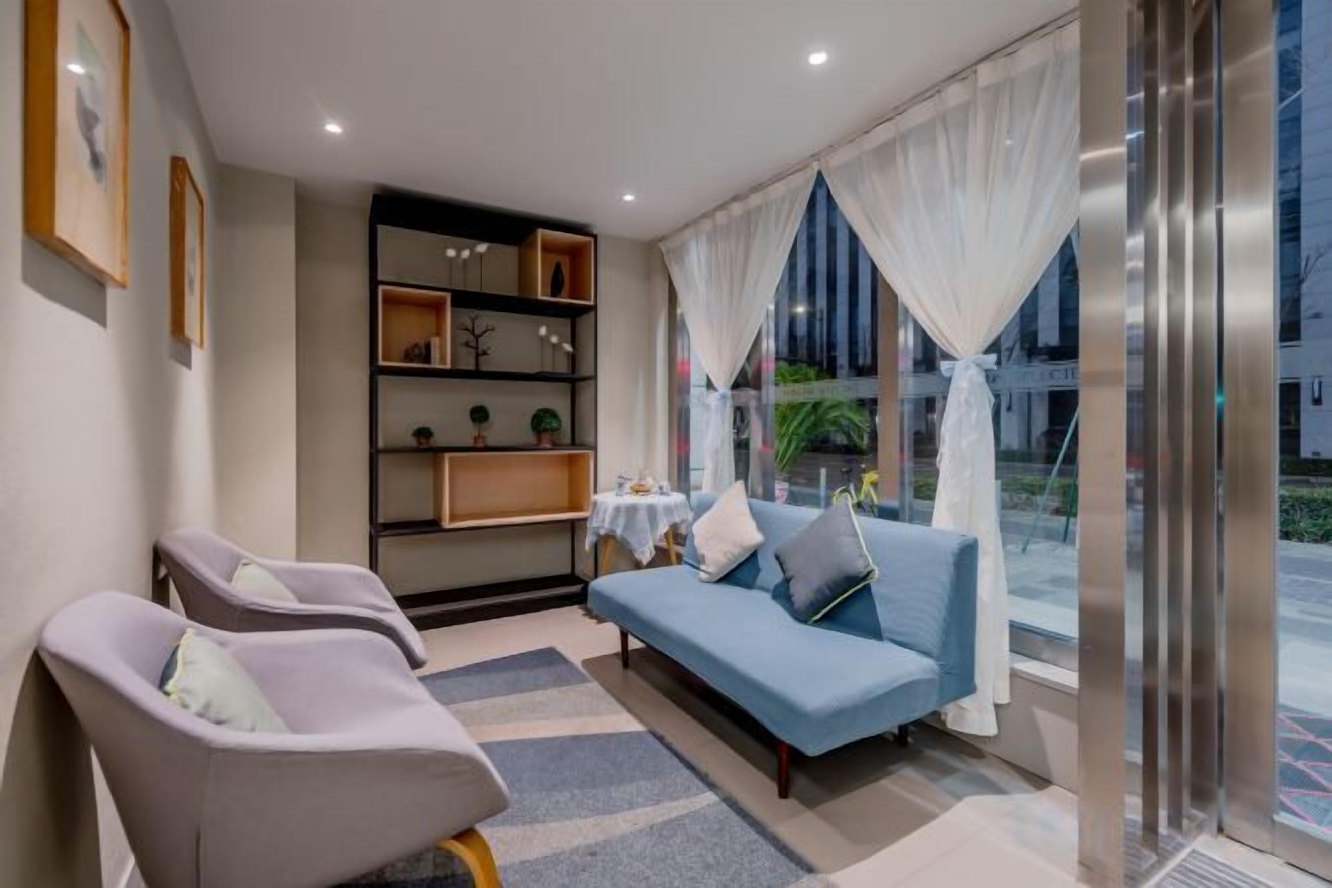 A modern living room with a sofa, two armchairs, a bookshelf, and a view through large windows.