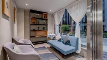 A modern living room with a sofa, two armchairs, a bookshelf, and a view through large windows.