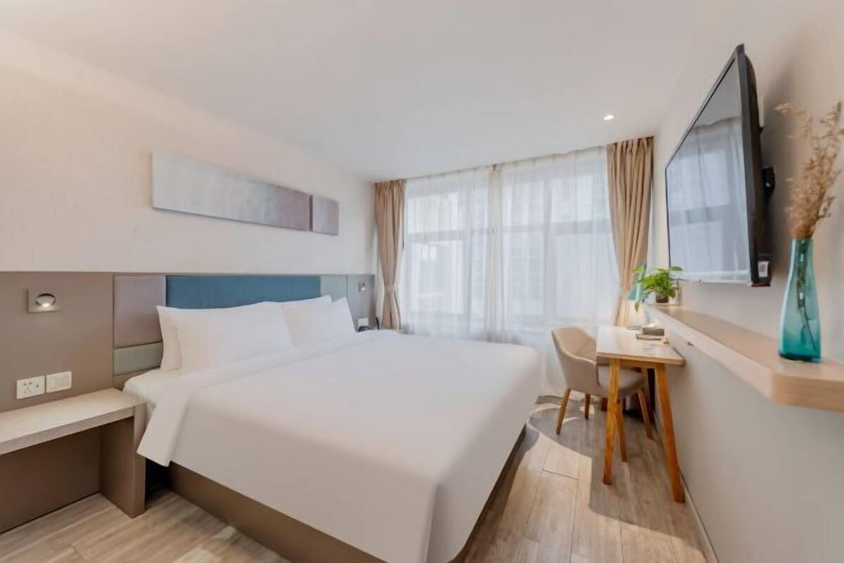 A hotel room with a bed, bedside table, desk, chair, and a TV mounted on the wall.