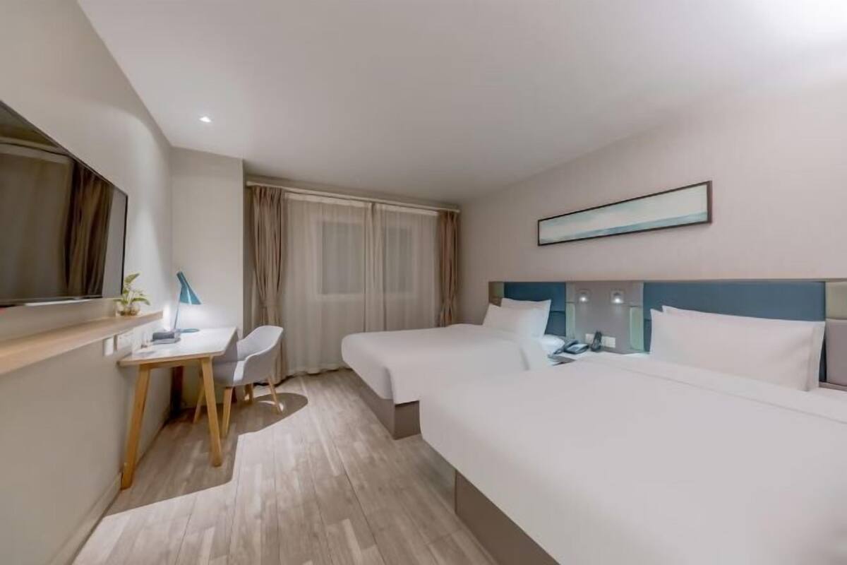 A hotel room with two beds, a desk, a chair, a mirror, and a window with curtains.
