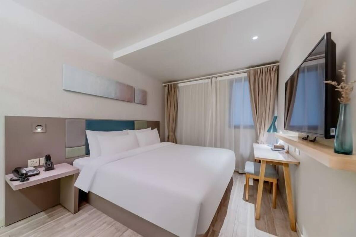 A hotel room with a bed, bedside table, TV, and a desk with a chair.