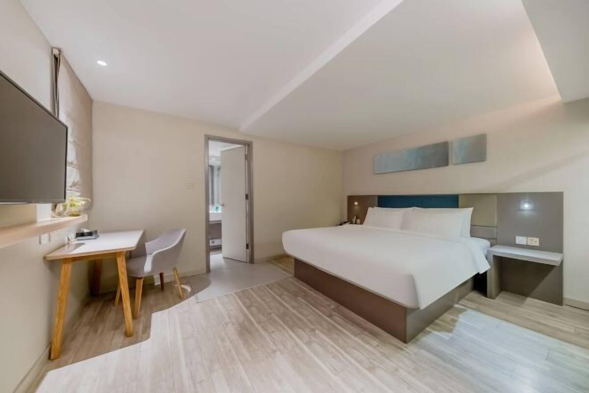 A modern hotel room with a bed, desk, chair, and a television.