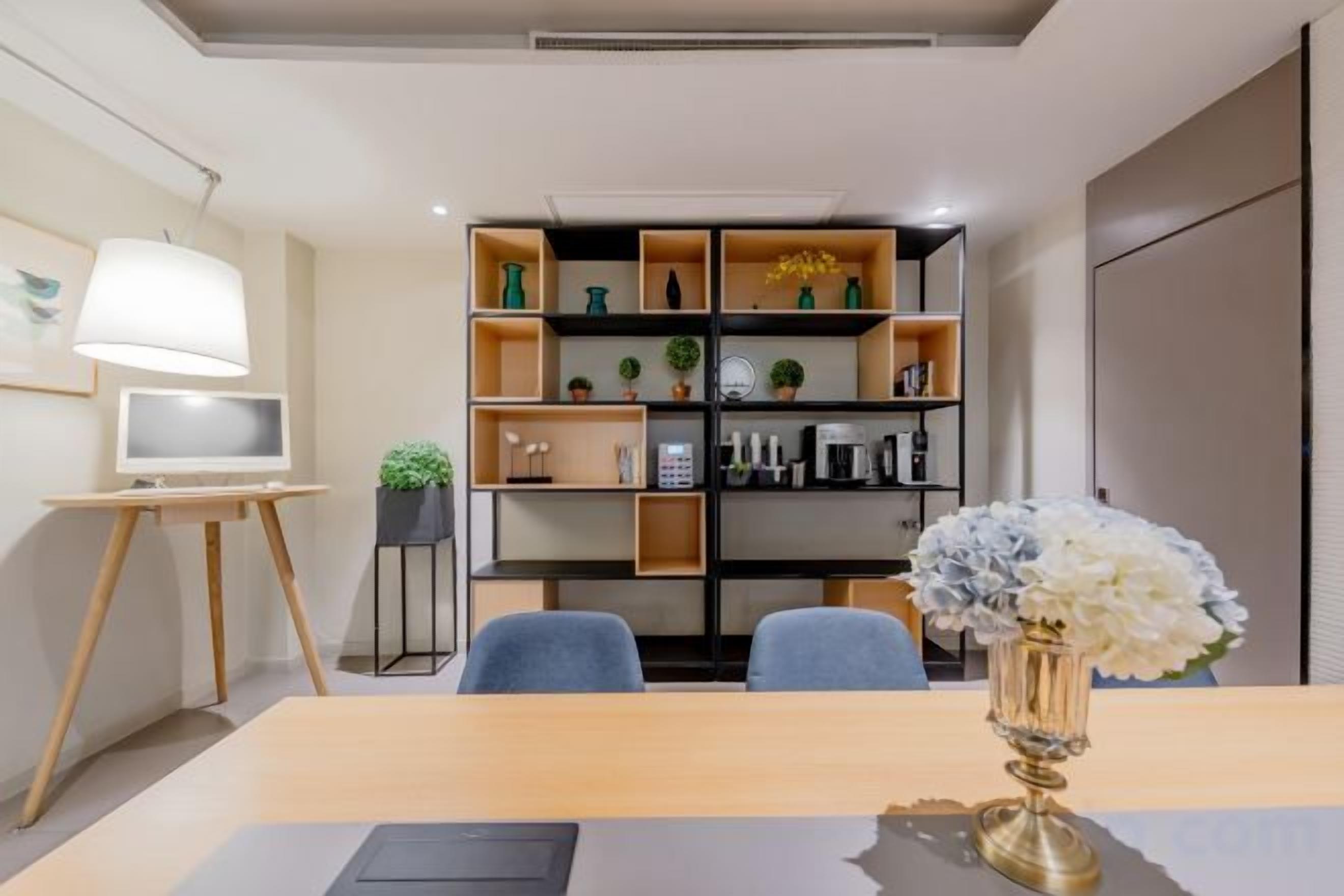 A modern room with a wooden dining table, two chairs, a TV on a stand, a bookshelf, and a potted plant.