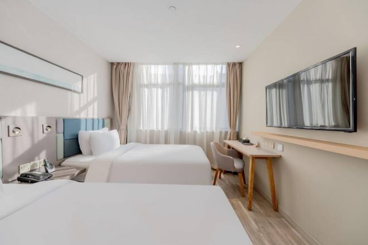 A hotel room with two beds, a desk, a chair, a TV, and a window with curtains.