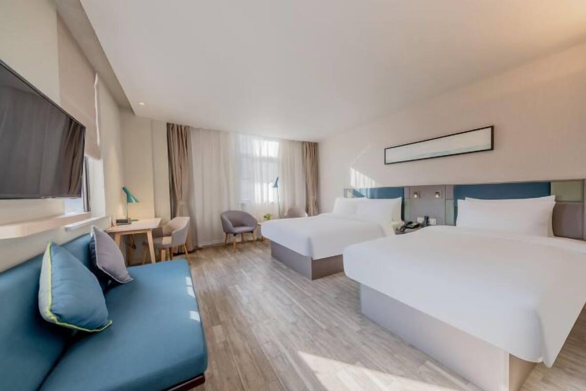A hotel room with two beds, a sofa, a desk, and a TV.