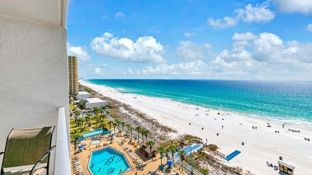 A beach resort with a swimming pool, beach umbrellas, and a view of the ocean.