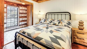 A bedroom with a stone wall, a bed with a geometric patterned bedspread, a wooden nightstand, and a window with a view of the outside. - Fire Pit, Views: Peaceful Texas Hill Country Cabin (Tarpley)
