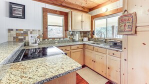 A kitchen with granite countertops, wooden cabinets, a built-in stove, and a window with a view of trees. - Fire Pit, Views: Peaceful Texas Hill Country Cabin (Tarpley)