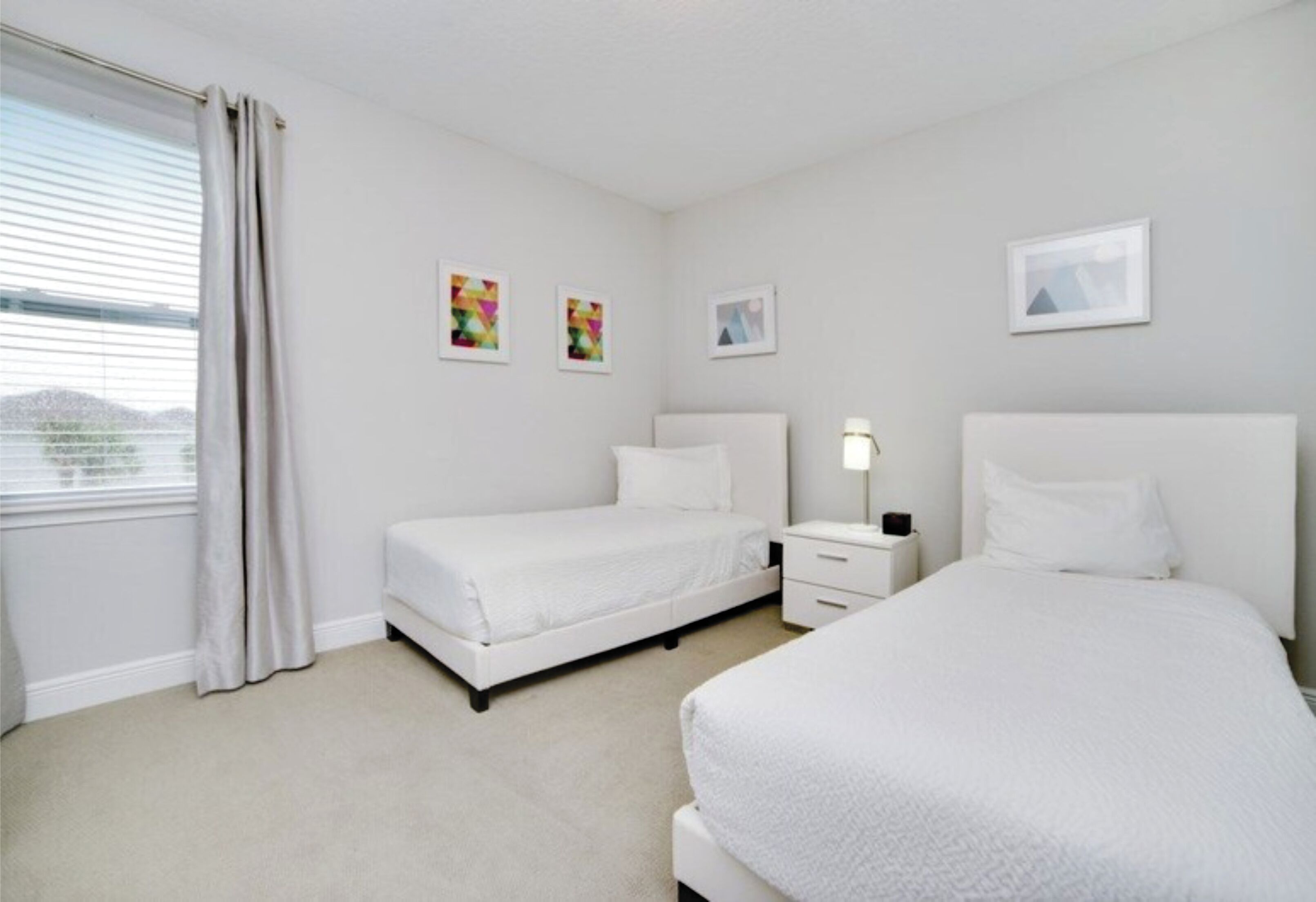 Une chambre d’hôtel avec deux lits simples, une table de chevet avec une lampe et une fenêtre avec des rideaux.
