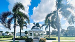 Um gazebo com cúpula de vidro, rodeado por palmeiras e um gramado bem cuidado.