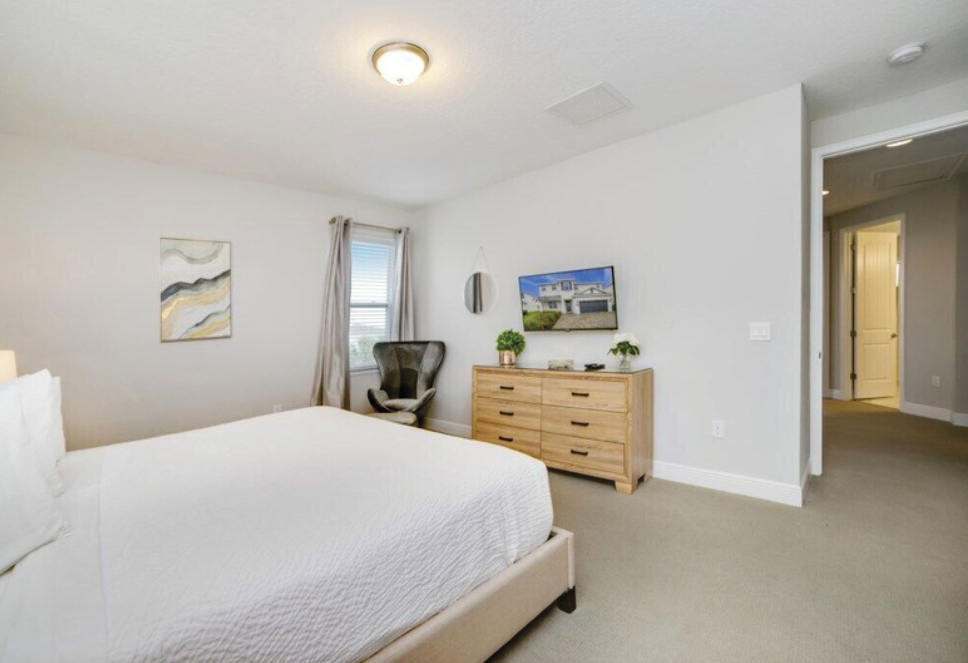 A bedroom with a large bed, a dresser, a chair, and a painting on the wall.