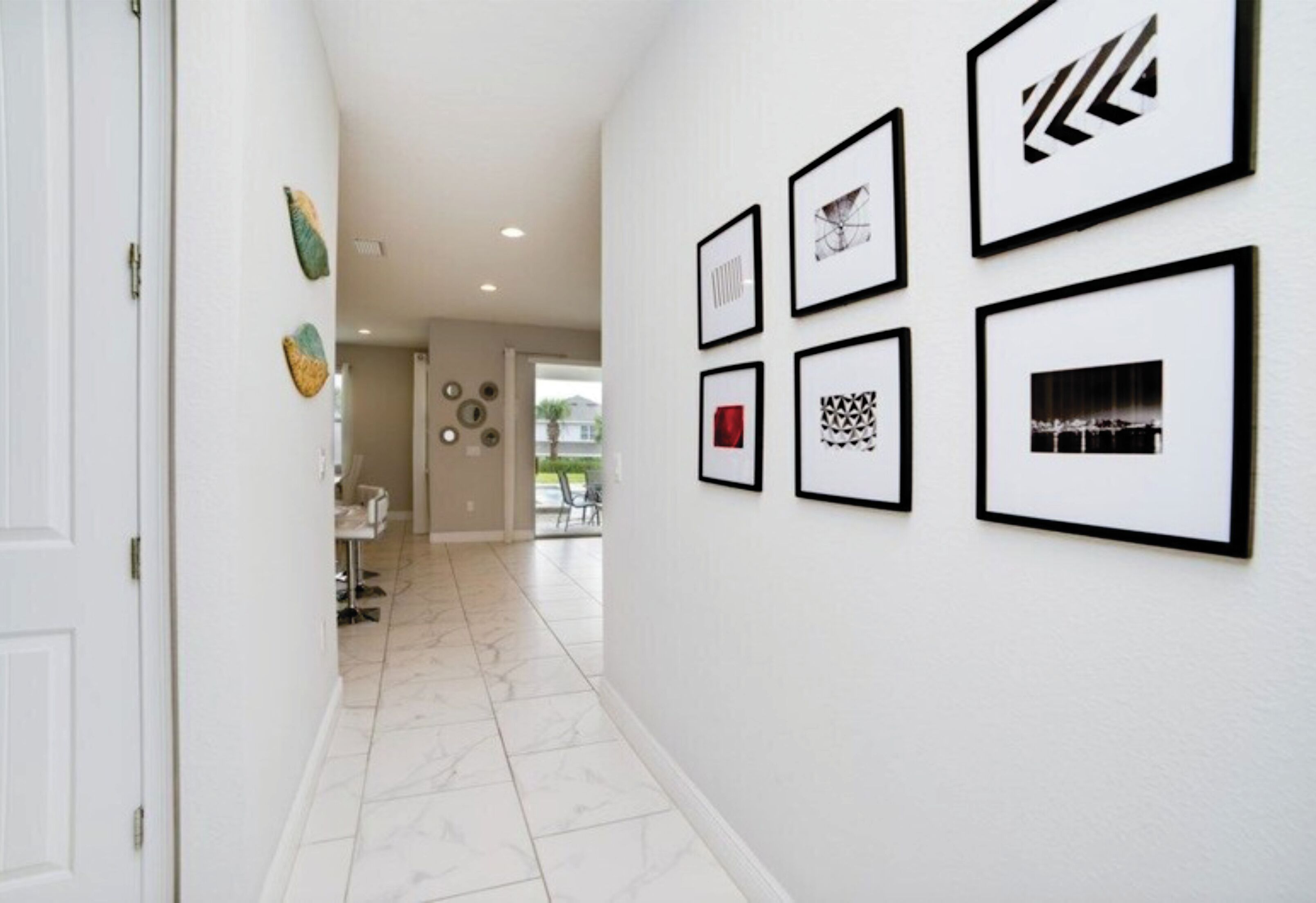 A hallway with a white door, a tiled floor, and six framed artworks on the wall.