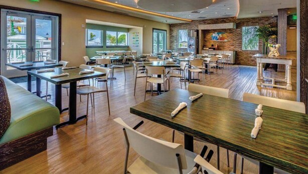 Um restaurante espaçoso com várias mesas e cadeiras, janelas amplas e um design de interiores moderno.
