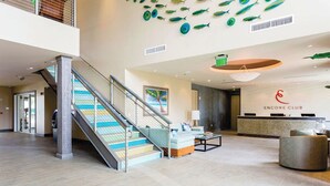 Um saguão de hotel com uma mesa de recepção, uma escadaria e um painel decorado com peixes.