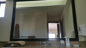 A bathroom with a large mirror, a sink with two faucets, a towel, and a soap dispenser. - The Grand Mayan at Vidanta! 1 BR studio! (Acapulco)