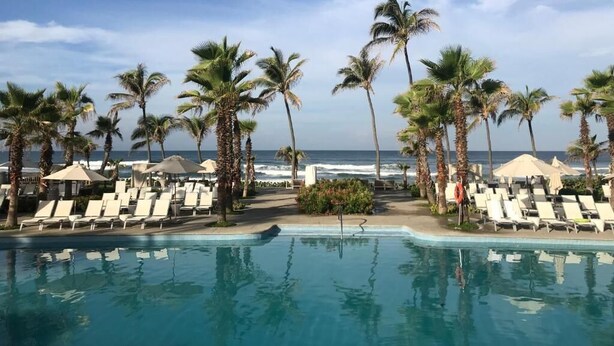 A poolside area with lounge chairs and palm trees, overlooking the ocean. - The Grand Mayan at Vidanta! 1 BR studio! (Acapulco)