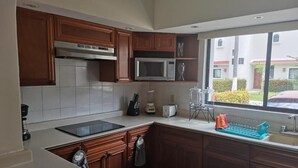 A kitchen with wooden cabinets, a microwave, a toaster, and a window with a view of a building and greenery outside. - The Grand Mayan at Vidanta! 1 BR studio! (Acapulco)