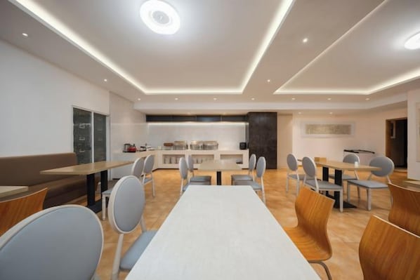 Un comedor moderno con una mesa larga y sillas, una cocina al fondo y un rincón de estar con un banco.