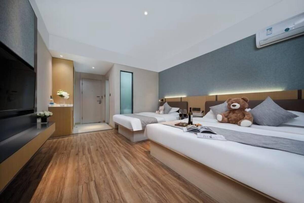 Une chambre d’hôtel moderne équipée d’un canapé-lit, d’une télévision, d’un ours en peluche et d’une table de chevet avec une bouteille et des verres.