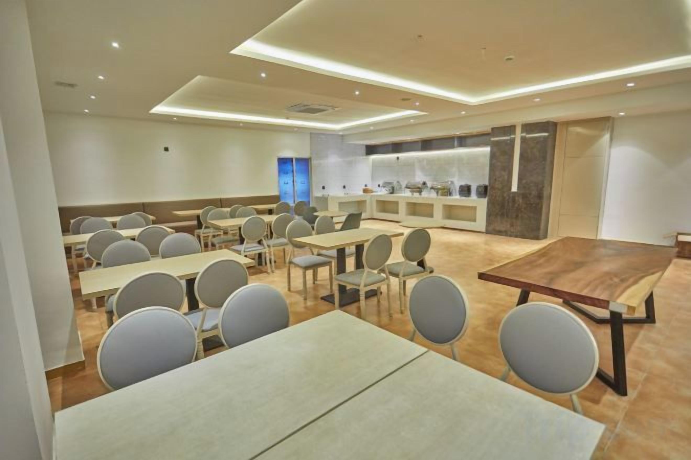 Een vergaderzaal met meerdere tafels en stoelen, een grote houten tafel en een toonbank met een presentatie.