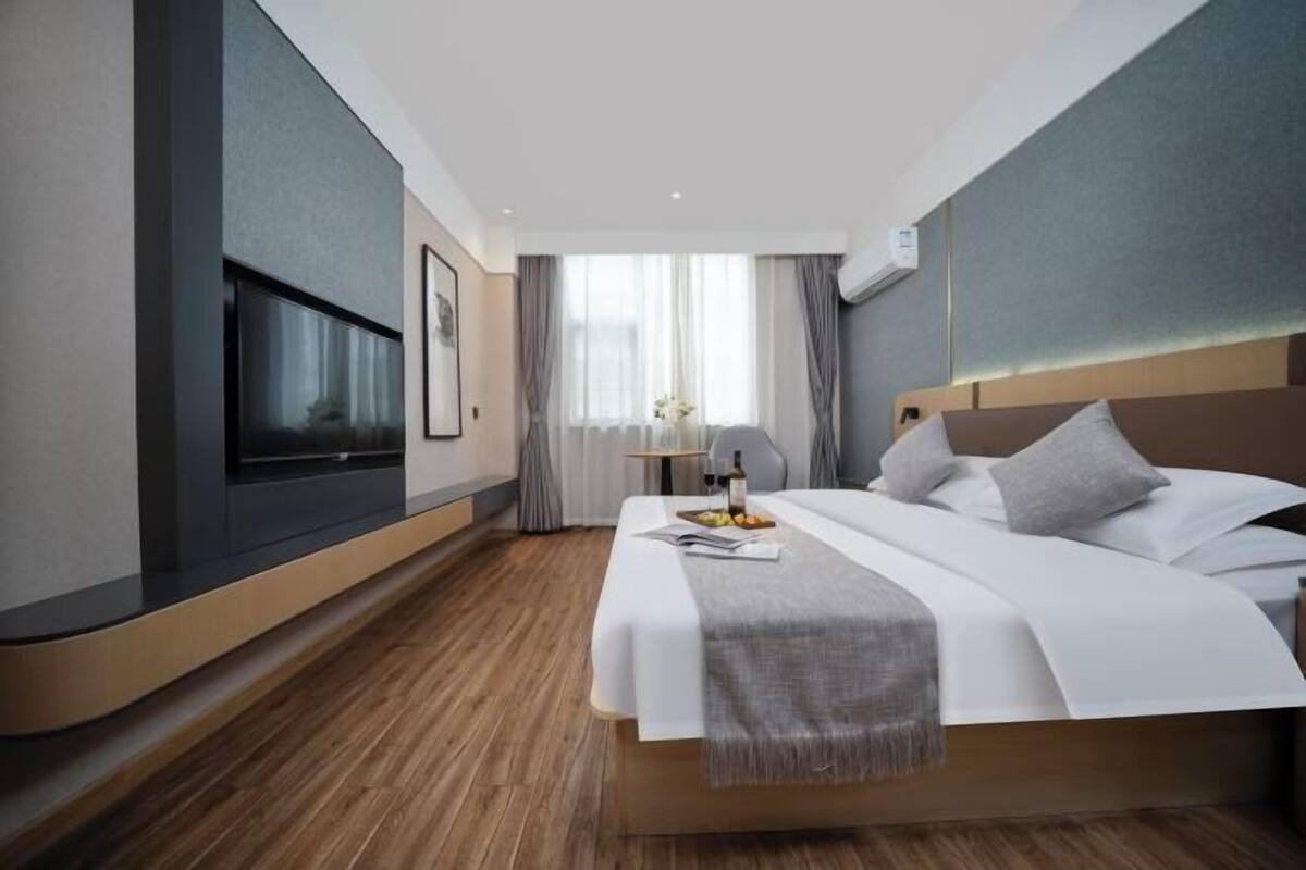Une chambre d’hôtel moderne dotée d’un grand lit, d’une télévision à écran plat, d’une table de chevet avec une lampe et d’une fenêtre avec des rideaux.