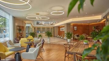 A modern hotel lobby with wooden flooring, round tables, and comfortable seating.