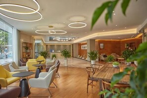 Una hall d'hotel moderna con pavimento in legno, tavoli rotondi e sedute confortevoli.