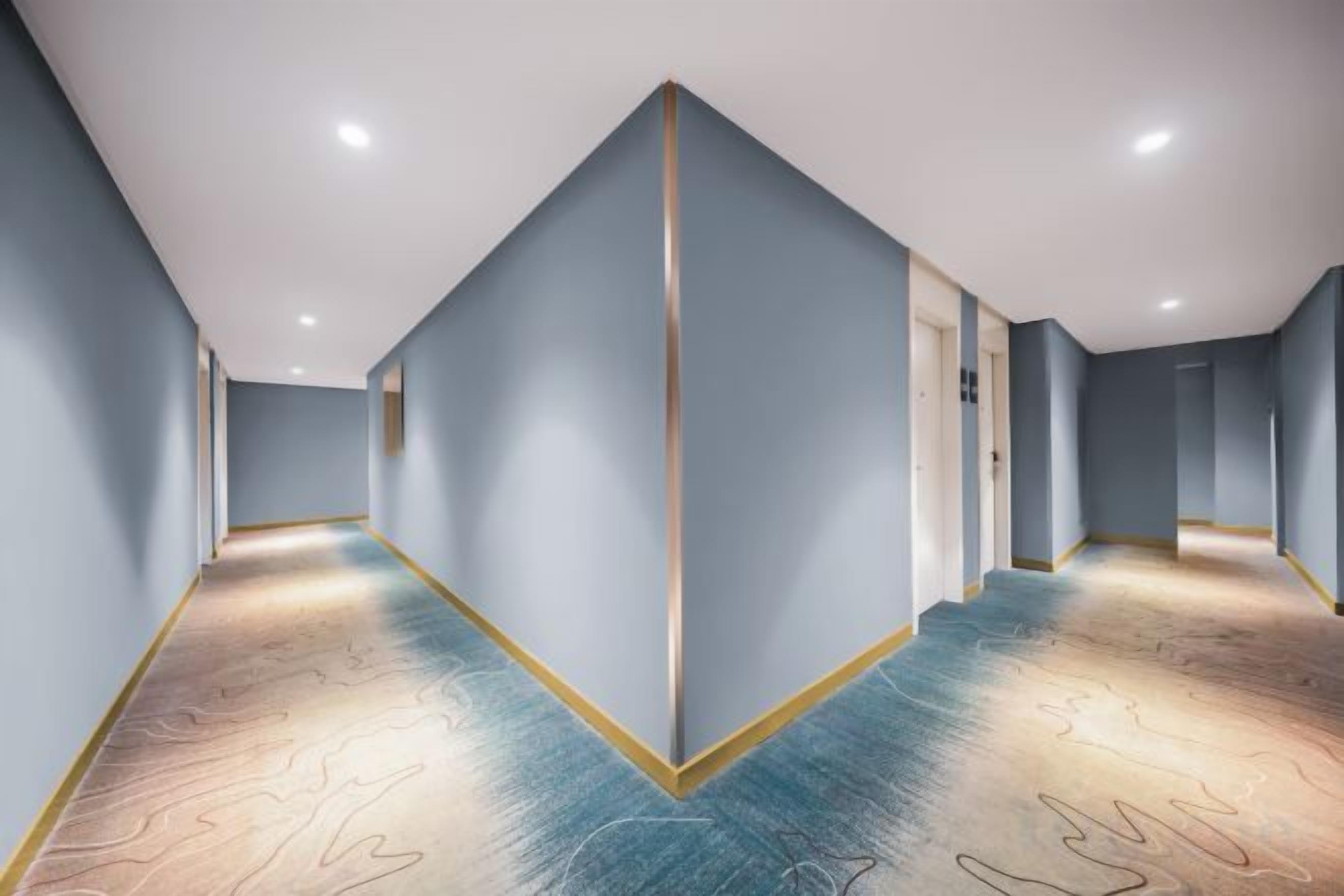 A corridor with a geometric floor pattern, light blue walls, and a central vertical line.