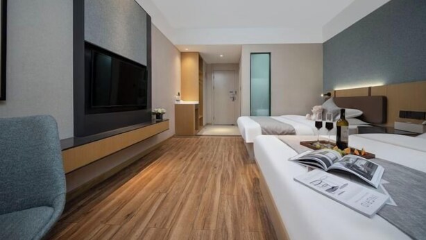 Ein modernes Hotelzimmer mit Fernseher, Sofa, Bett, Nachttisch und einem kleinen Tisch mit Zeitschrift und Flasche.