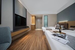A modern hotel room with a TV, a sofa, a bed, a bedside table, and a small table with a magazine and a bottle. - Shiji Xinghe Hotel (Huangshan Tunxi Old Street) (Huangshan City)