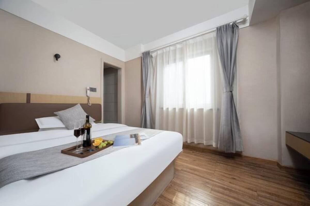 Une chambre d’hôtel avec un grand lit, une table de chevet, une fenêtre avec des rideaux et un plancher en bois.