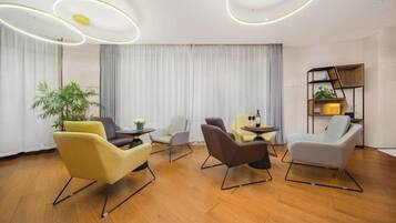A modern hotel room with a wooden floor, a large window with curtains, and a seating area with chairs and a small table.