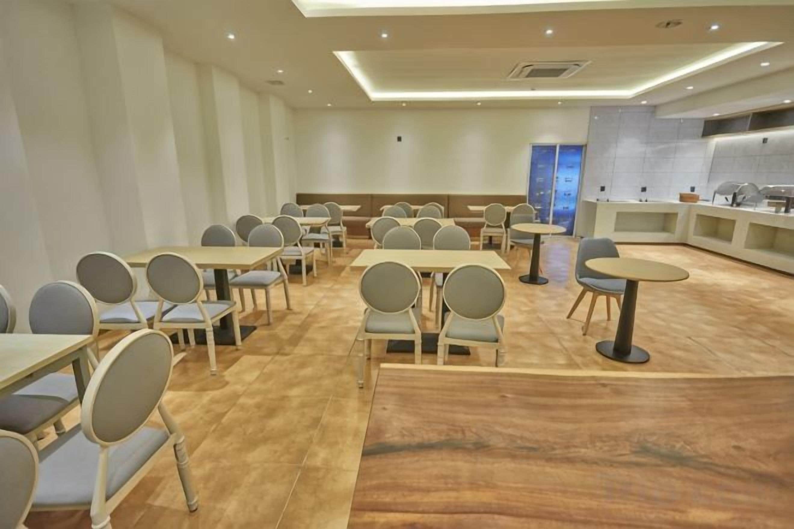 A conference room with multiple tables and chairs, a kitchen area, and a view of the cityscape.