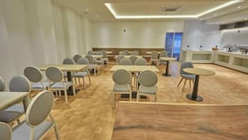 A conference room with multiple tables and chairs, a kitchen area, and a view of the cityscape.