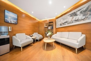 A modern living room with a sofa, two armchairs, a coffee table, and a water dispenser. - Shiji Xinghe Hotel (Huangshan Tunxi Old Street) (Huangshan City)
