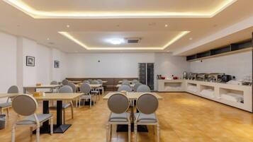 A modern dining area with tables and chairs, a kitchen area with appliances, and a seating area with a sofa.