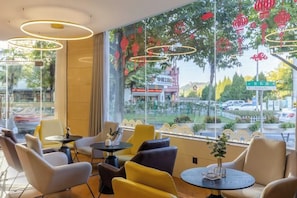 A cafe with round tables and chairs, large windows with decorative elements, and a view of the street outside. - Shiji Xinghe Hotel (Huangshan Tunxi Old Street) (Huangshan City)