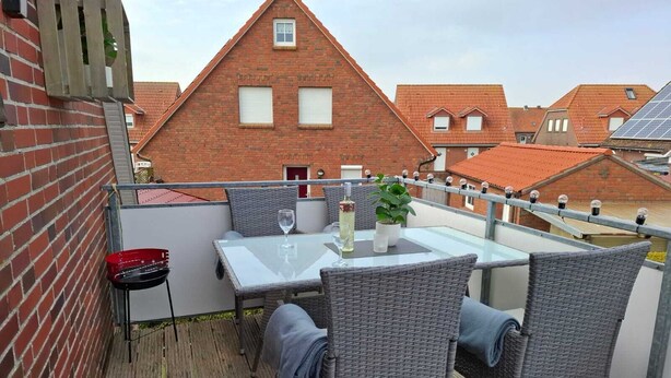 Une terrasse sur le toit avec une table en verre, des chaises en osier, un barbecue rouge et une plante en pot.