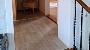 Un couloir avec un plancher en bois, une chaise en osier et une armoire en bois.