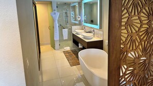 Un baño moderno con ducha de mampara de vidrio, dos lavamanos, un espejo grande y una bañera independiente.
