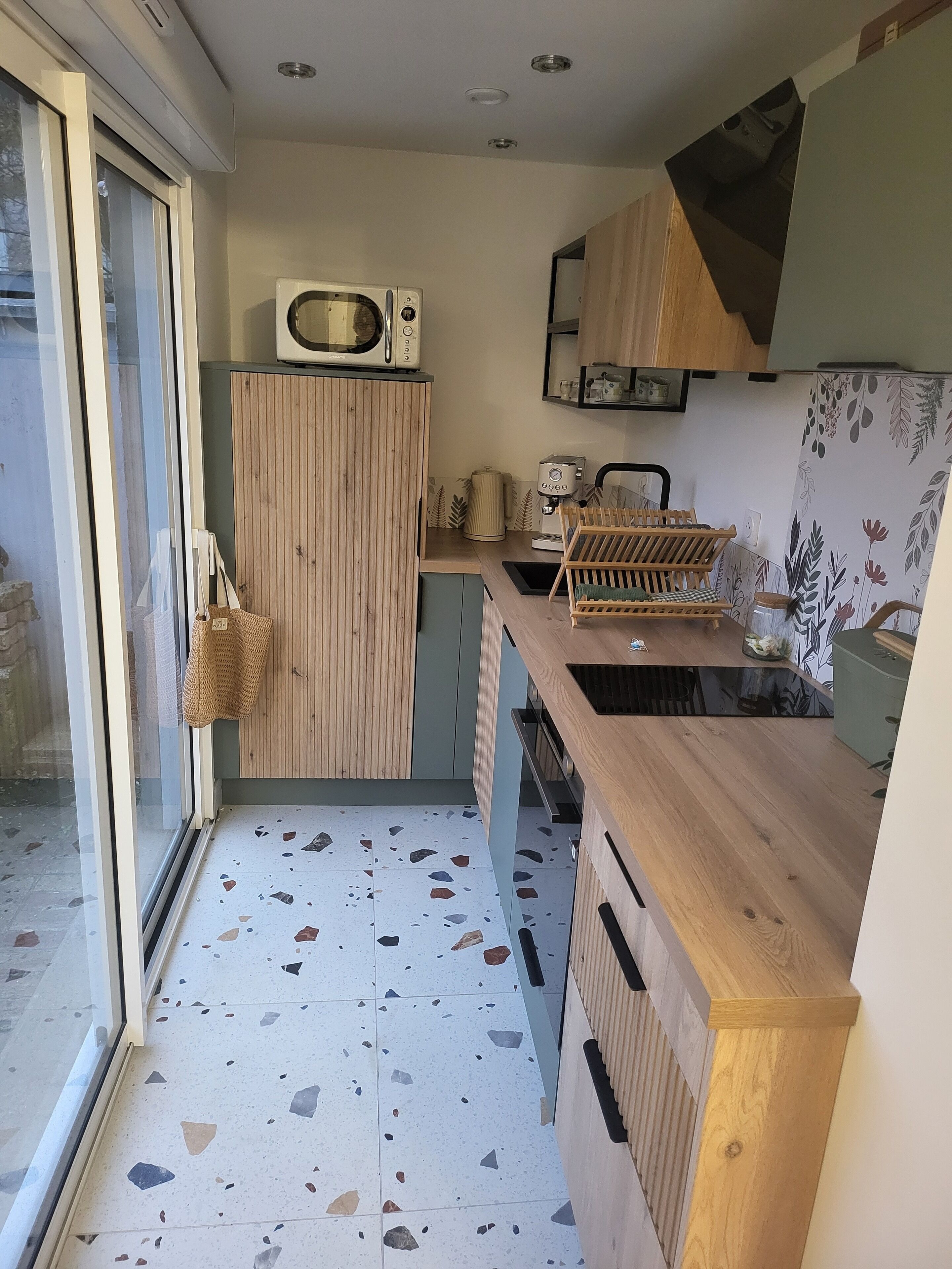 Ett kompakt kök med ett träskåp, en mikrovågsugn, en kaffemaskin och ett litet handfat.